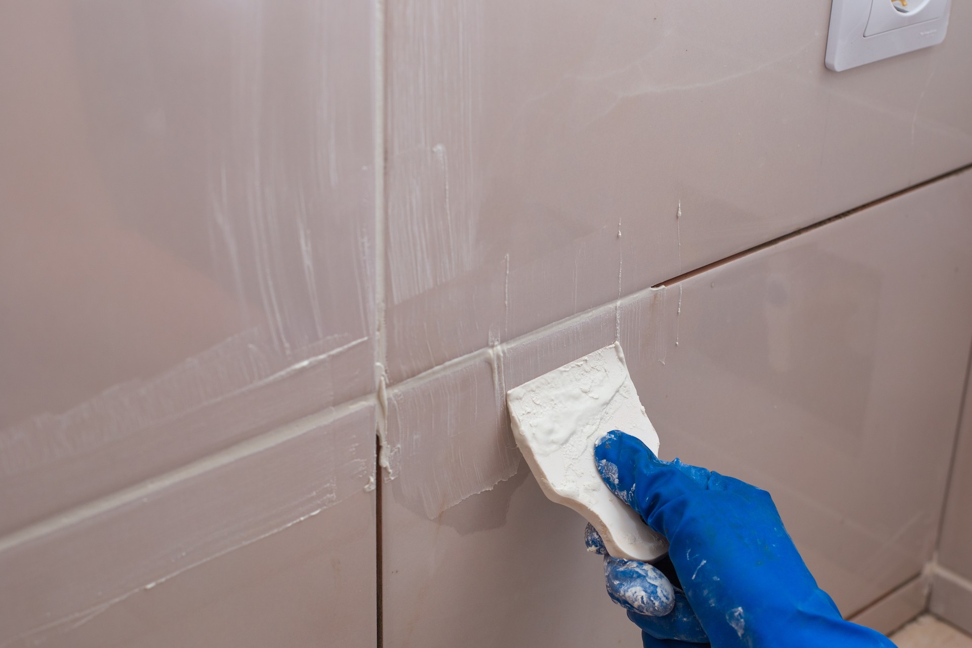 Repair and wall cladding with tiles. The master rubbing the tile joints with a white putty with a rubber spatula